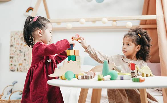 Two young children playing with colourful wooden blocks in a childcare centre.